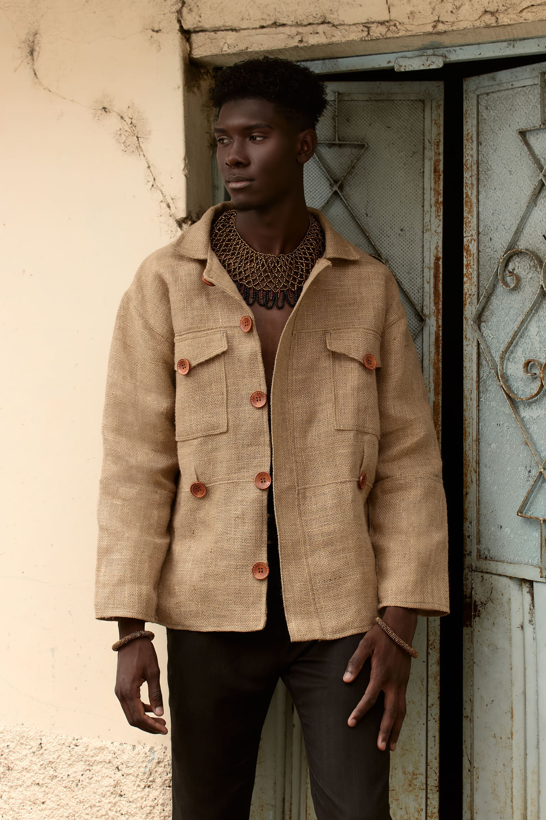 Editorial Coangue: hombre con chaqueta artesanal beige y collar de chaquira en un portal de piedra.